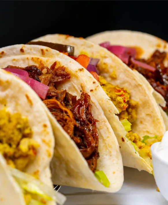 four soft beef tacos filled with shredded meat, pickled red onions, and fresh yellow salsa.