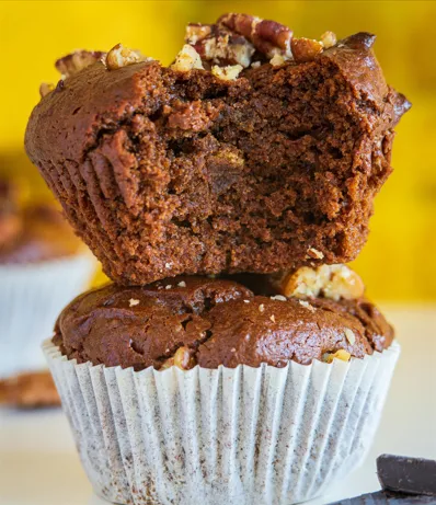 A stack of two moist chocolate muffins topped with chopped pecans, with the top muffin showing a soft, crumbly interior.