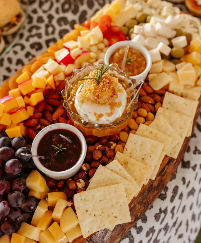 A colorful gourmet cheese board with crackers, burrata topped with honey, grapes, nuts, and fruit preserves.